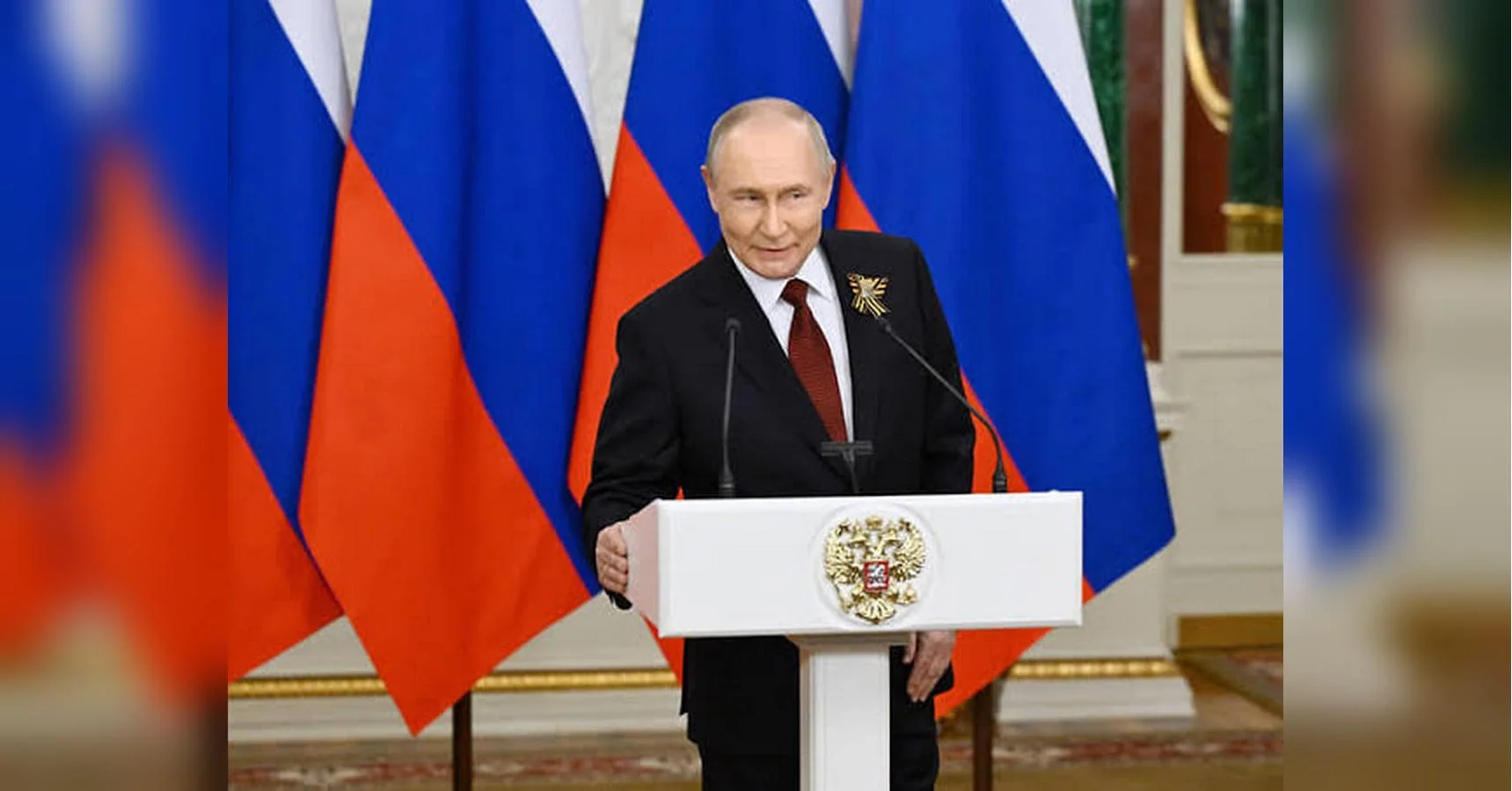 Володимир Путін виступає за трибуною з гербом на тлі російських прапорів